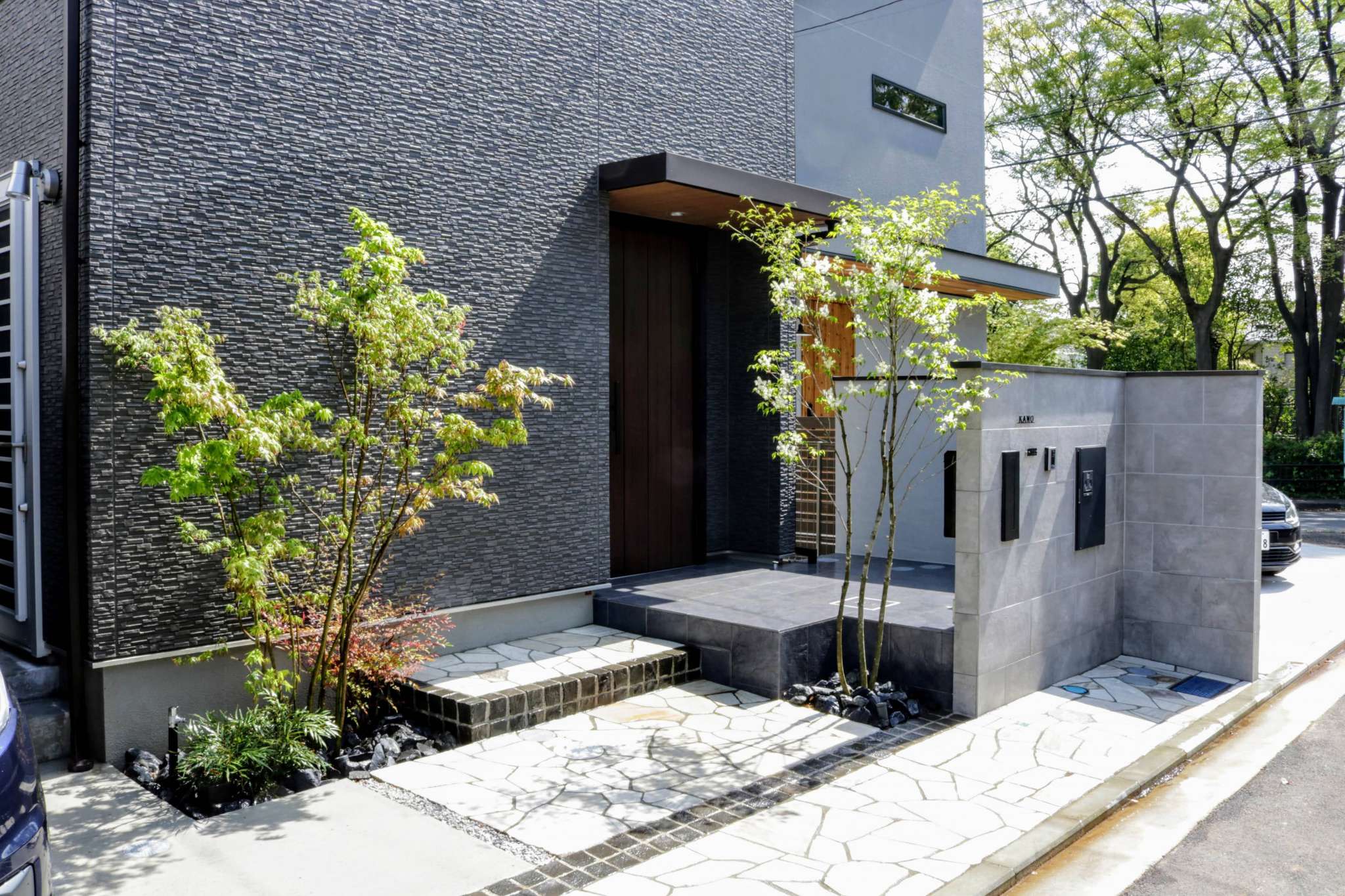 シンボルツリーの間を抜ける石張りのアプローチと拡張された玄関ポーチ