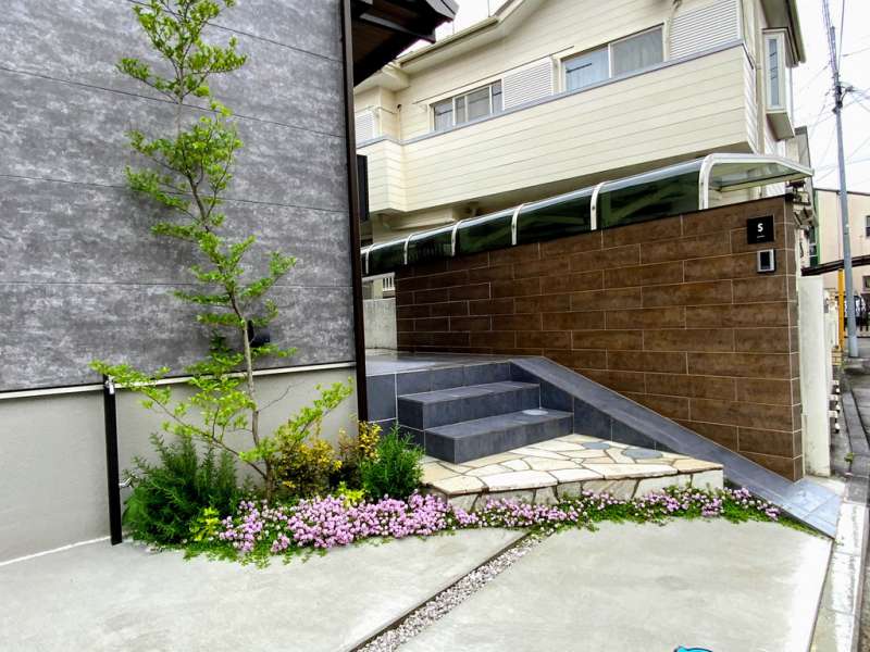 木目調タイル貼りの門袖、趣のある樹形のエゴノキ。ピンクの花はクリーピングタイム。